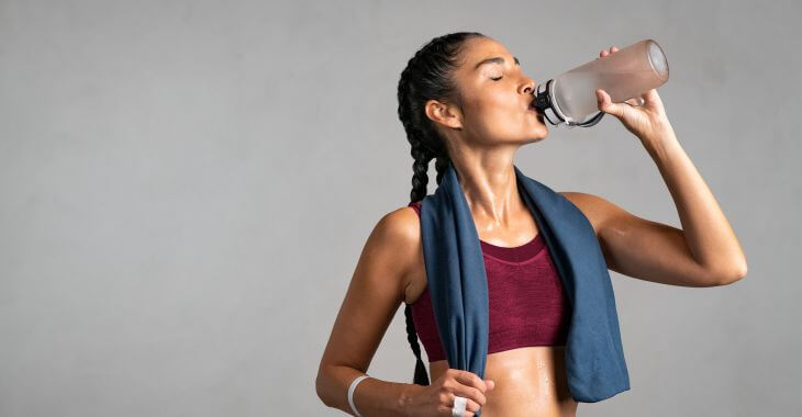 A woman in fitness clothes drinking water during a workout.