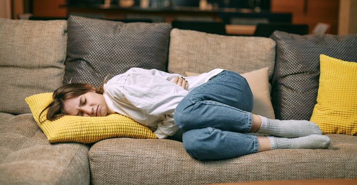 A young woman suffering from abdominal and cramps lying on a sofa.