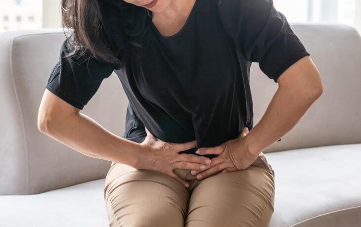 A woman suffering from abdominal and cramps sitting on a sofa. 
