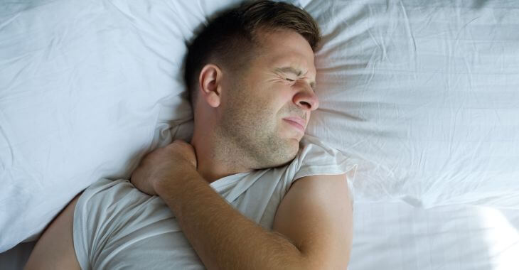 A man in the bed woken up by a shoulder pain