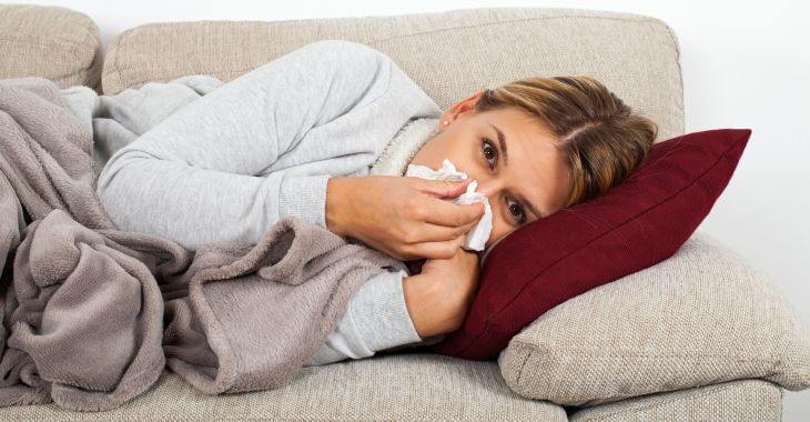 A sick woman suffering from sinus infection lying on a couch. 