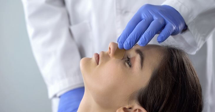 Plastic surgeon examining nose of a woman after rhinoplasty surgery.