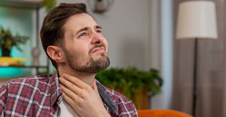 A man suffering from throat issues and voice problems touching his neck