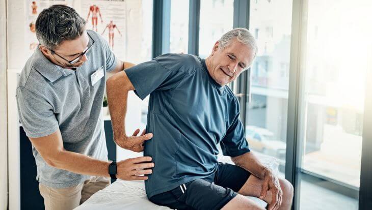 A physical therapist consulting an elderly man with lower back pain
