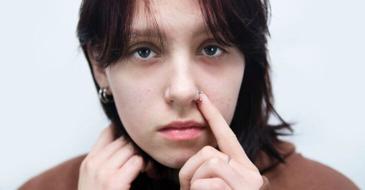 A concerned teenage girl touching a pierced area on her nose.