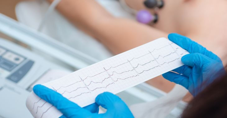 A doctor revising an ECG test results standing next to a patient with electrodes placed on his chest