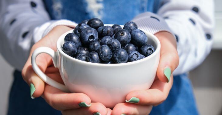 hands of a woman holding a big cup full of blueberries