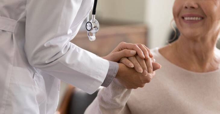 a primary care doctor holding a hand of an elderly woman and talking to her