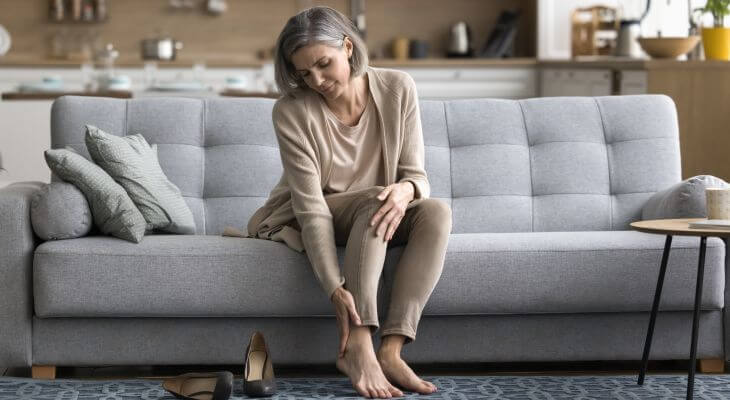 A concerned middle-aged woman sitting on a couch and looking at her bare feet