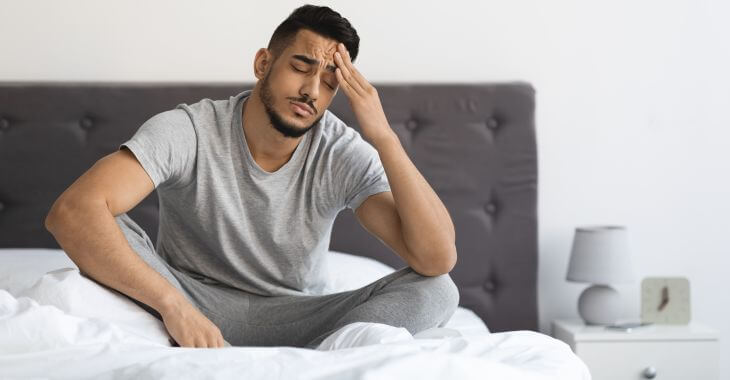 A fatigued man feeling headache after waking up