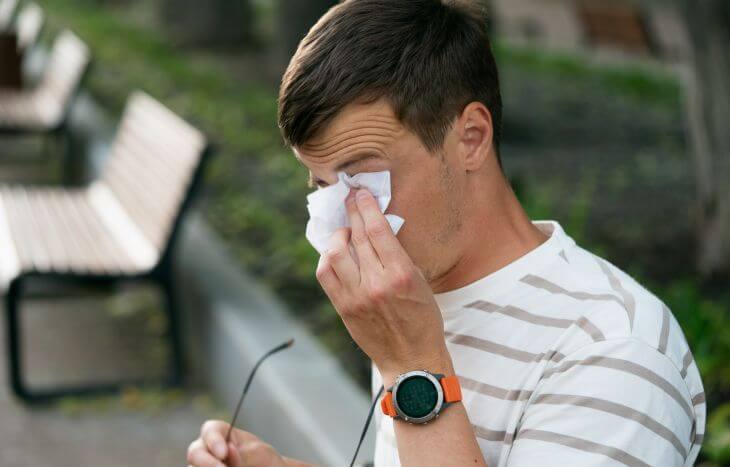 A man wiping a tearing eyes caused by a seasonal allergy