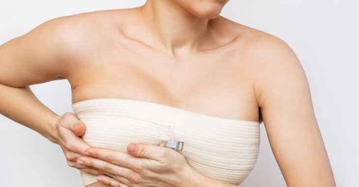 A woman after breast plastic surgery with elastic bandage around her breasts during the recovery time