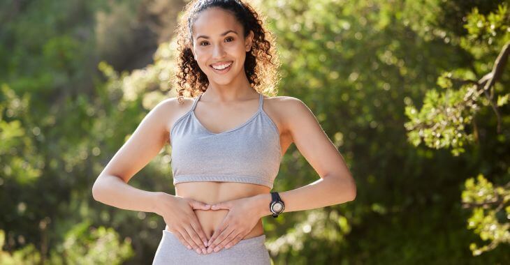 Happy energetic young woman in sports clothes holding putting hands in the shape of heart over her stomach