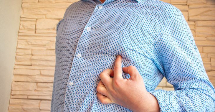 a torso of a man wearing blue shirt pointing at his breast and nipple