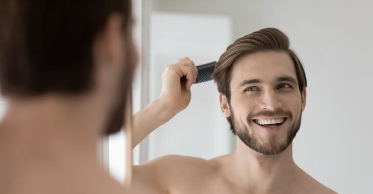 Happy man combing his thick strong hair in fron of a mirror.