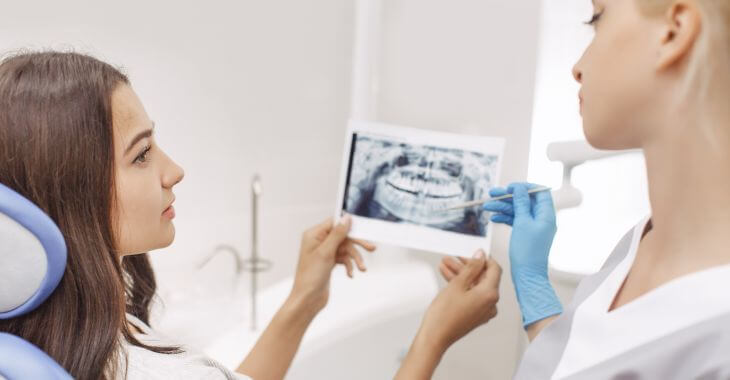 A female dentist showing X-rays to a woman sitting in a dental chair and explaining her the treatment 