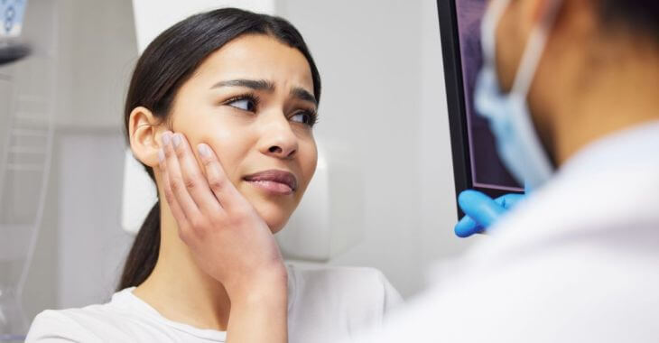 A dentist showing patient the dental imaging and explaining root canal procedure to a woman with a dental pain
