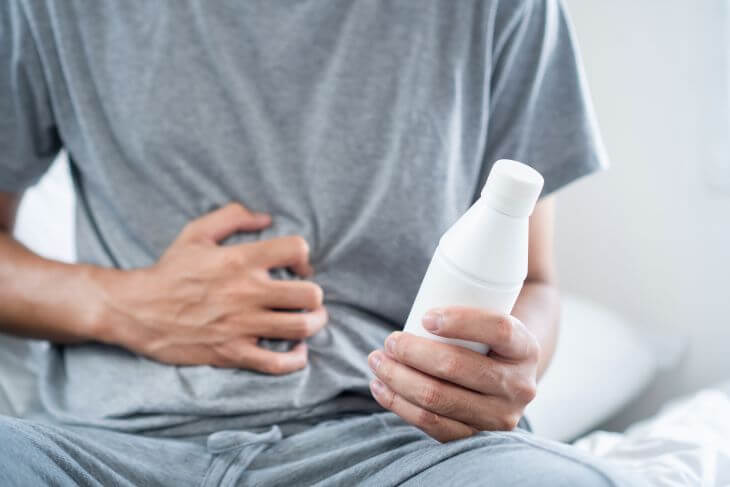 Man feeling burning sensation caused by acid reflux holding a bottle with medication