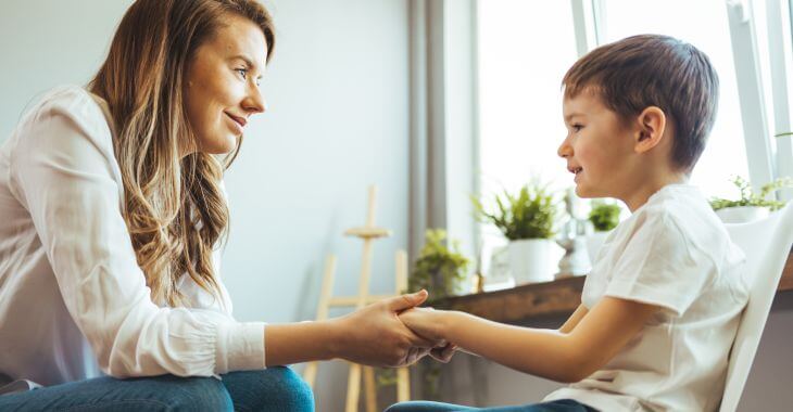 A mother sitting opposite her little son with speech delay problems , holding his hands and looking at his face