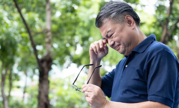 Concerned mature Asian man ubbing his eyes