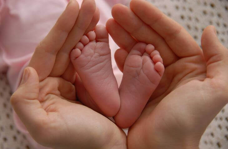 Hands of a woman holding gently newborn's feet