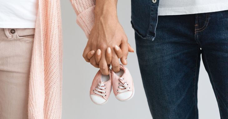 Man a woman walking holding hand. They are together holding babie's shoes betweene them.