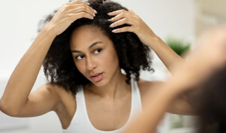 An Afro_American woman with thick hair checking her skalp and baby hair in front of the mirror