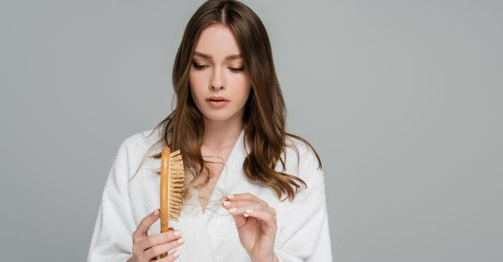 a concerned young woman in a bathrobe taking down a bunch of hairs from her hairbrush