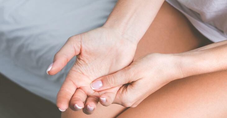 Woman suffering from hand pain and finger pain after sleep sitting on a bed and massaging painful hand