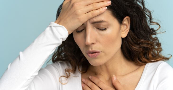 A fatigued woman with breath shortness feeling dizzy, and presses one hand to her chest and the other to forehead