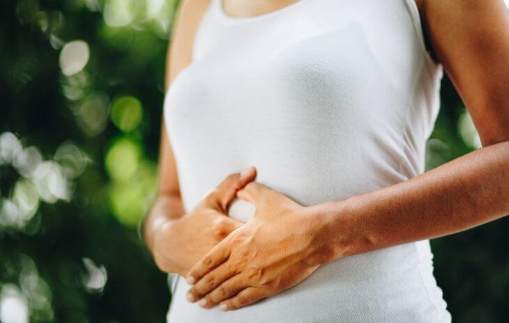 Relaxed woman spending time actively outdoors touching her stomach with both hands