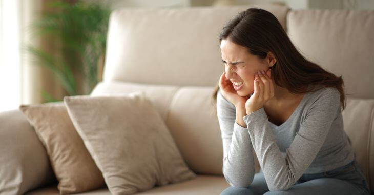 Young woman feeling strong jaw pain caused by TMJ