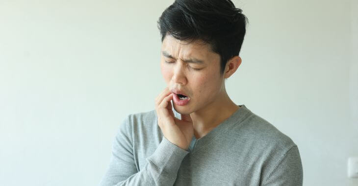 Asian man feeling jaw stiffness and pain due to TMJ 