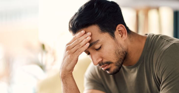 Fatigued man sitting with closed eyes and leaning his forehead on his hand
